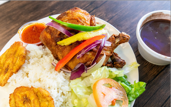 Plated dish with chicken, rice, salad, and plantains on a wooden table.