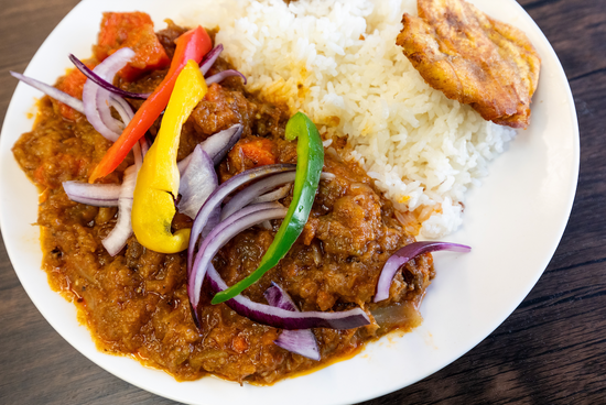 Plated dish with Haitian legim, rice, and vegetables on a white plate.