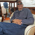 Man sitting inside a boat cabin wearing sunglasses and a gray sweater.