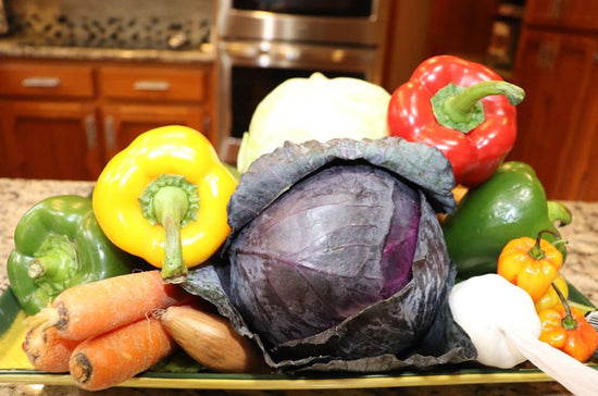 Assorted vegetables including peppers, carrots, and a cabbage on a kitchen counter.